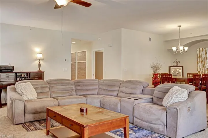Spacious carpeted living room with stylish pendant lighting and ceiling fan — move-in ready Cape Coral condo