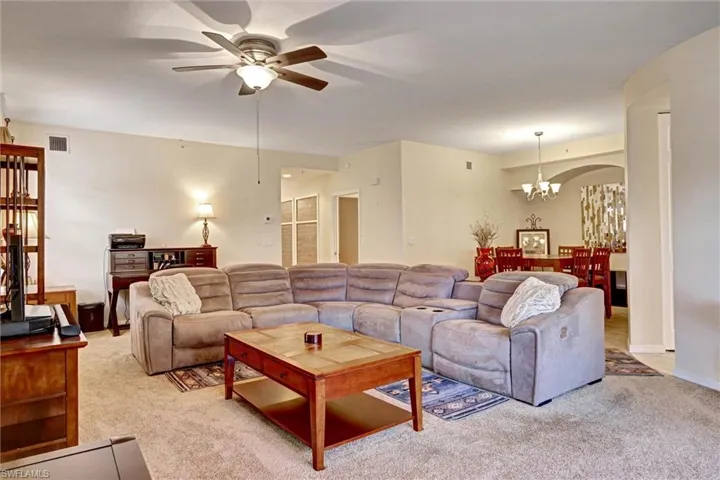 Elegant living room featuring chandelier, ceiling fan, and classic arched walkways adding architectural charm