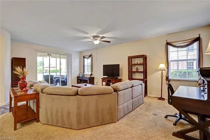 Bright and open living room with light-colored carpet, built-in desk nook, and ceiling fan — ideal Cape Coral condo layout