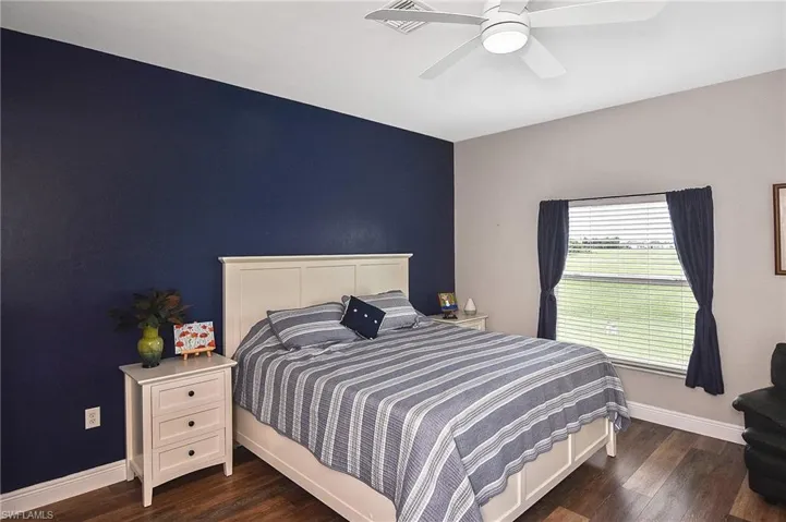 Bedroom featuring dark wood-style flooring, a ceiling fan, and an accent wall