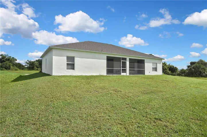 Rear view of house featuring a yard, stucco siding, and a sunroom