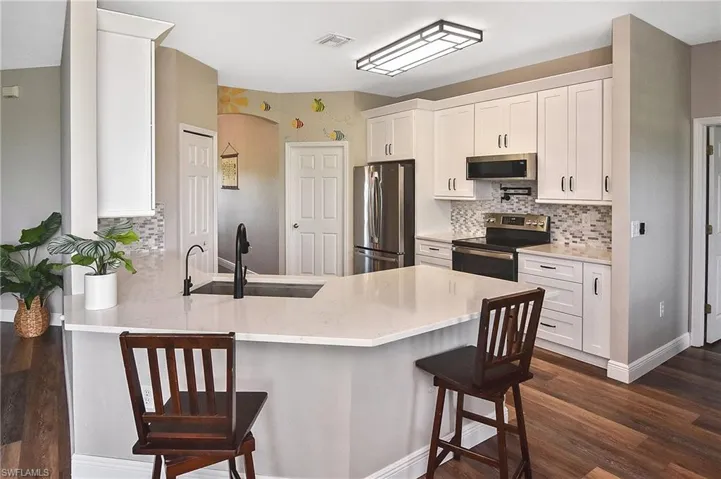 Kitchen featuring white cabinets, stainless steel appliances, a kitchen bar, and backsplash