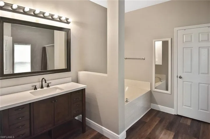 Full bathroom with a bath, vanity, and dark wood-style flooring