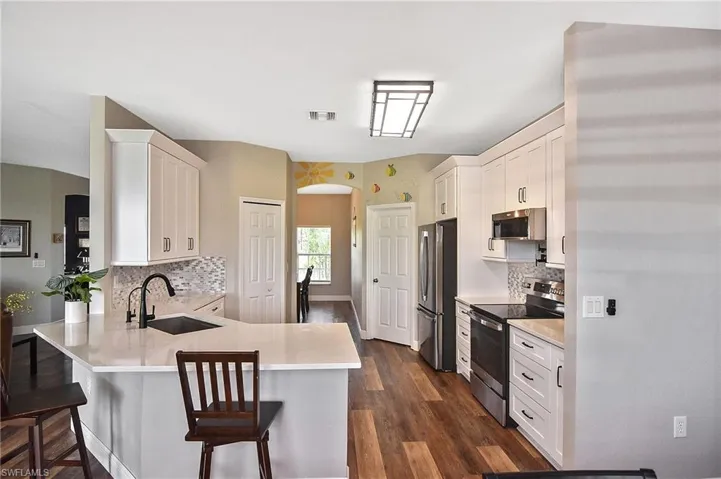 Kitchen featuring stainless steel appliances, arched walkways, a peninsula, white cabinetry, and tasteful backsplash