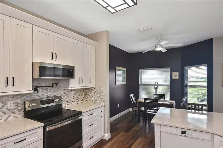 Kitchen with appliances with stainless steel finishes, white cabinets, light stone counters, ceiling fan, and tasteful backsplash