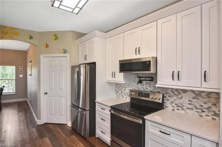 Kitchen featuring stainless steel appliances, arched walkways, white cabinetry, backsplash, and dark wood-type flooring