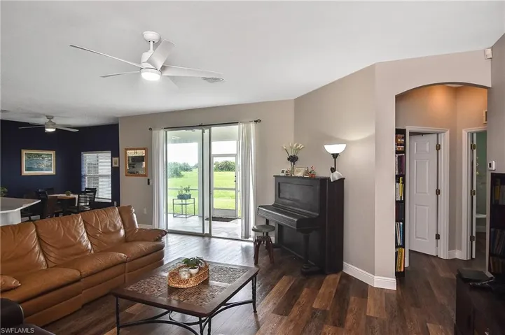 Living room with arched walkways, dark wood-type flooring, and ceiling fan
