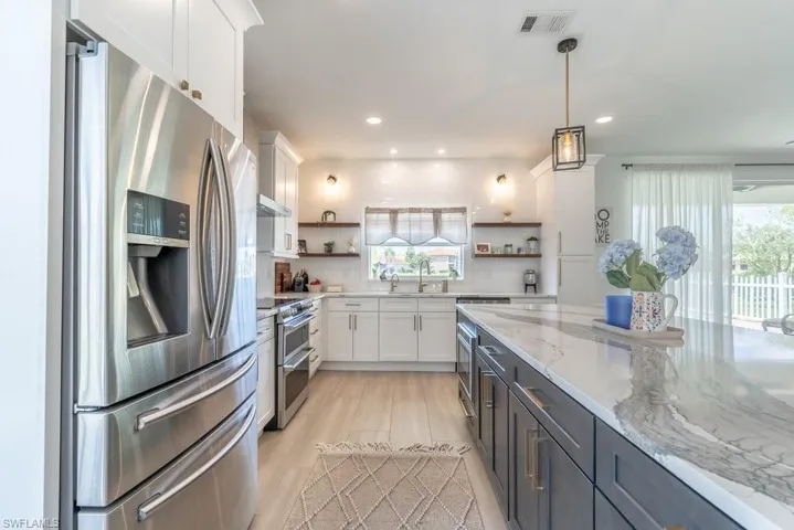 Kitchen featuring stainless steel appliances, open shelves, white cabinetry, light stone countertops, and hanging light fixtures