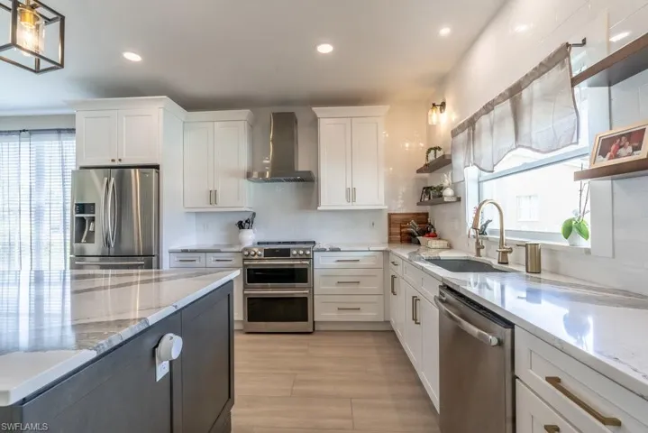 Kitchen with appliances with stainless steel finishes, wall chimney range hood, open shelves, white cabinets, and recessed lighting