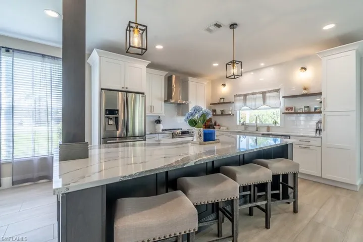 Kitchen featuring appliances with stainless steel finishes, open shelves, wall chimney exhaust hood, decorative backsplash, and white cabinetry