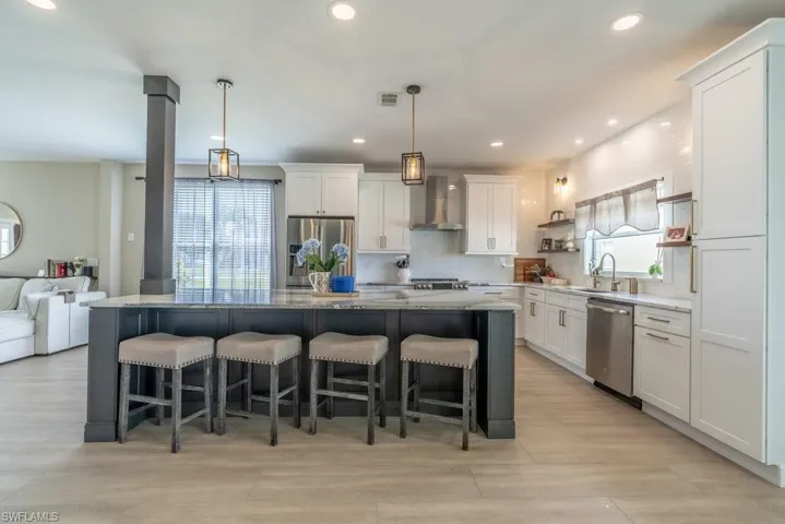 Kitchen featuring appliances with stainless steel finishes, wall chimney range hood, white cabinetry, a spacious island, and recessed lighting