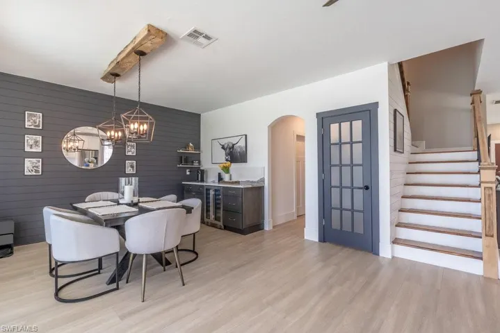 Dining area with wine cooler, arched walkways, light wood-style flooring, a chandelier, and wood walls