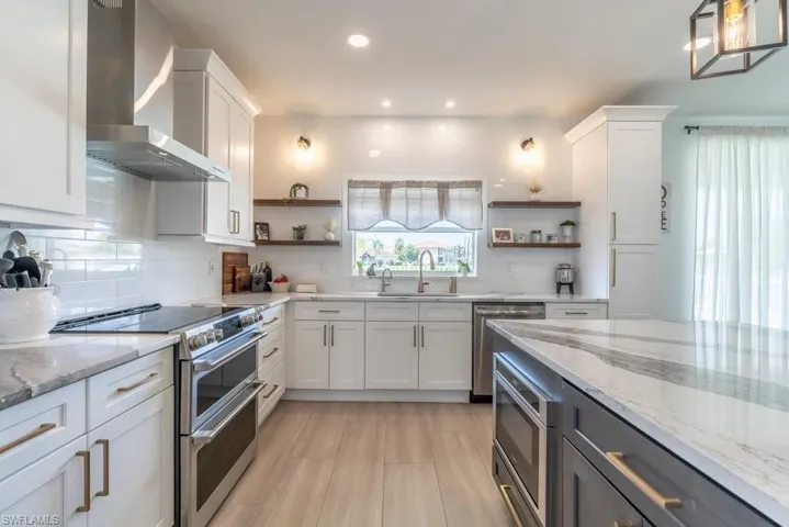 Kitchen featuring wall chimney range hood, stainless steel appliances, open shelves, white cabinetry, and recessed lighting