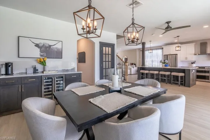 Dining space with beverage cooler, light wood-type flooring, stairs, arched walkways, and recessed lighting