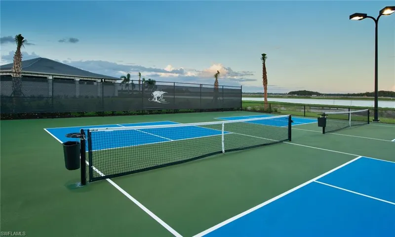 View of tennis court with basketball hoop and a water view