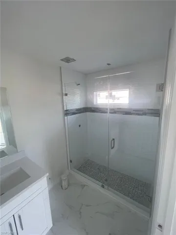 Bathroom with a shower with shower door, tile flooring, plenty of natural light, and vanity