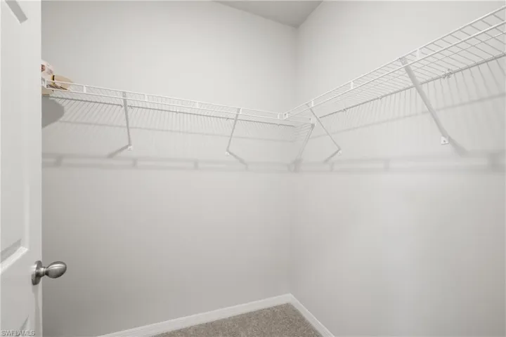Master walk in Corner closet with ample wire shelving and a hanging rod, featuring neutral wall paint and carpet flooring