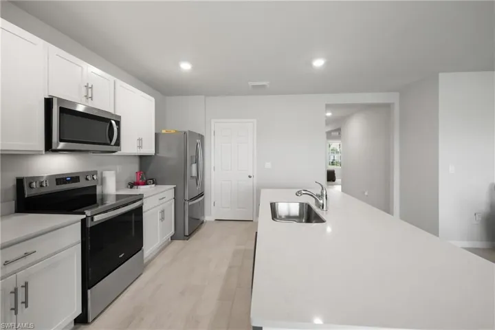 Modern kitchen featuring white shaker cabinetry, stainless steel appliances, light wood-finish flooring, a spacious island with an undermount sink, and recessed lighting