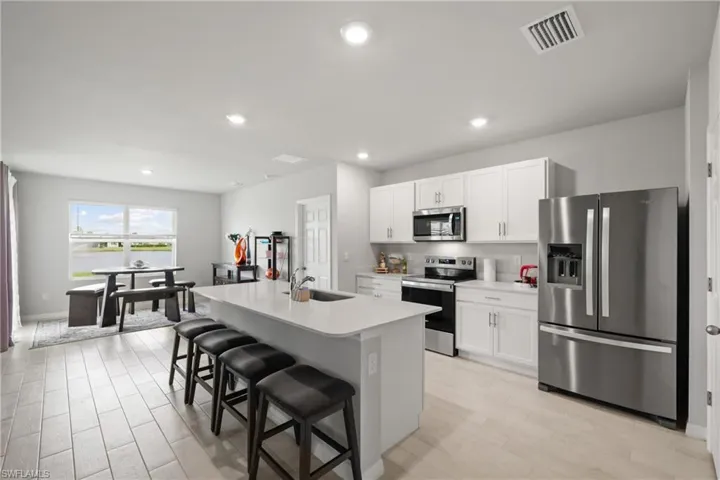 Open-concept kitchen and dining area featuring a central island with seating, stainless steel appliances, white cabinetry, and wood-finish flooring