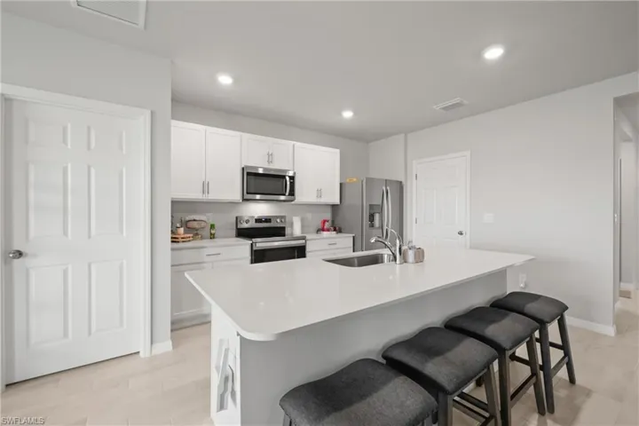 Modern kitchen featuring a large island with an undermount sink, white shaker cabinetry, stainless steel appliances, and light-toned flooring