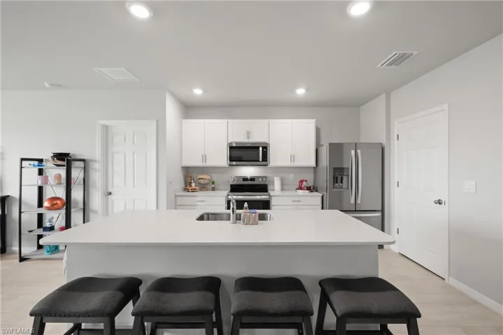 Modern kitchen featuring an expansive island with an undermount sink, white cabinetry, a white tile backsplash, stainless steel appliances, and recessed lighting