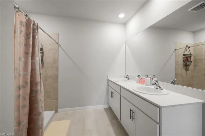 Double vanity with white cabinetry and integrated sinks, a full-width mirror, and overhead recessed lighting