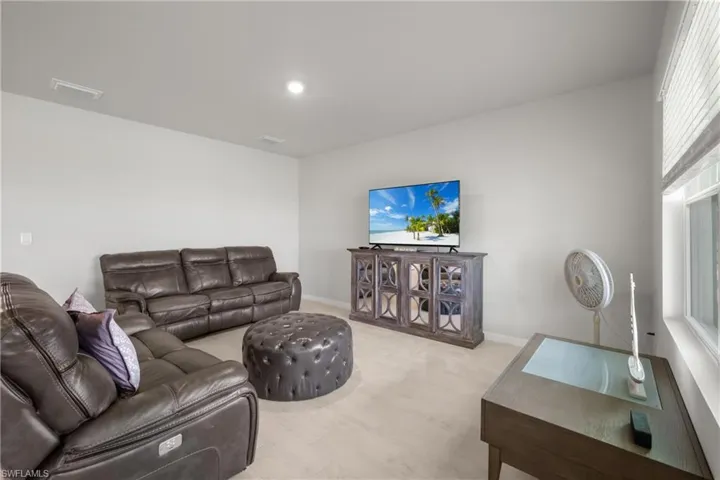 Carpeted entertainment area featuring light gray walls, recessed lighting, and a window with horizontal blinds