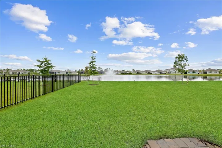 Expansive green lawn with a black metal fence, overlooking a water feature with a fountain
