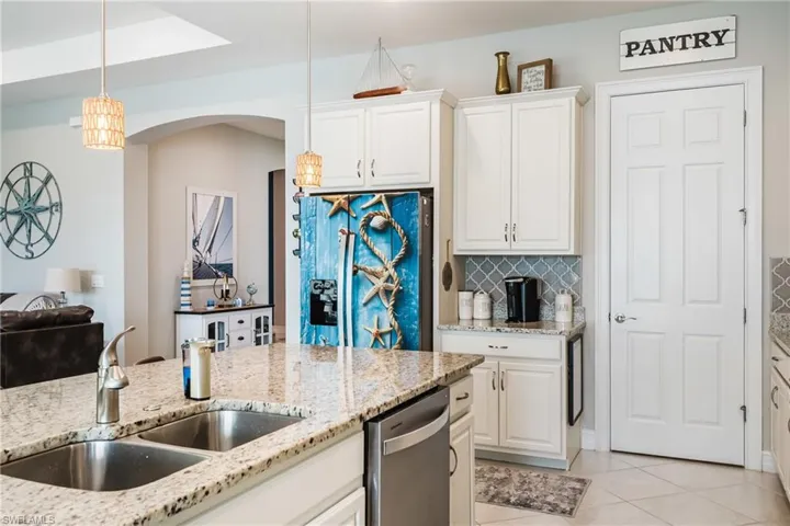 Kitchen with backsplash, arched walkways, white cabinetry, light tile patterned flooring, and light stone counters