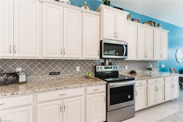 Kitchen featuring appliances with stainless steel finishes, light stone counters, backsplash, light tile patterned flooring, and white cabinets