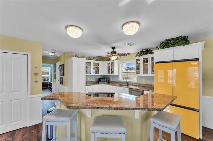 Kitchen with white cabinets, stainless steel dishwasher, dark hardwood / wood-style floors, fridge, and a breakfast bar area