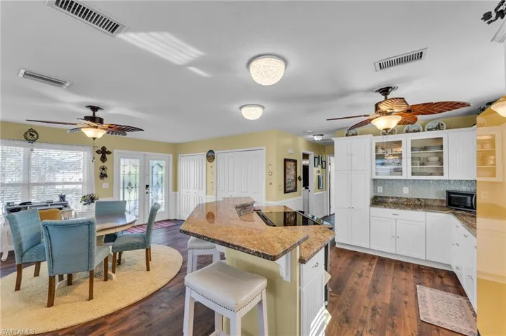 Kitchen featuring dark hardwood / wood-style flooring, backsplash, black appliances, white cabinets, and a breakfast bar area