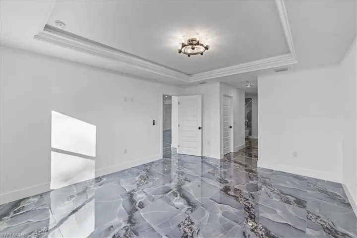 Spare room with marble tiled flooring, crown molding, and a raised ceiling