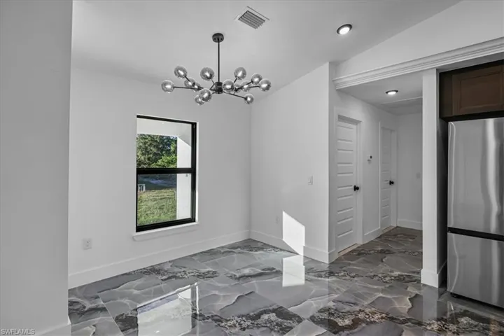 Unfurnished dining area featuring a chandelier, dark marble finish flooring, and vaulted ceiling
