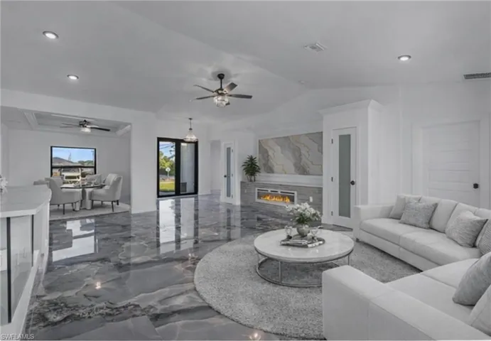 Living room featuring marble tiled flooring, recessed lighting, a glass covered fireplace, vaulted ceiling, and a ceiling fan
