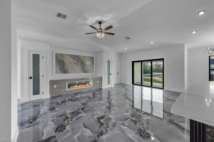 Living room with dark marble finish floors, a glass covered fireplace, lofted ceiling, ceiling fan, and recessed lighting