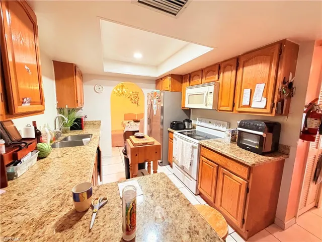 Kitchen featuring wood finish cabinetry, white appliances, arched walkways, light tile patterned flooring, and a tray ceiling
