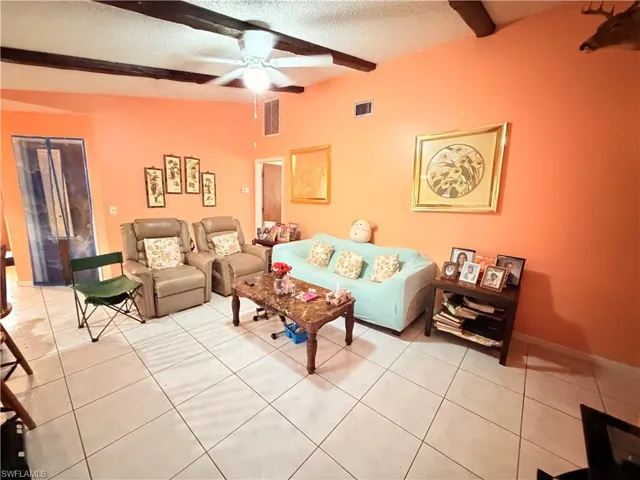 Living room featuring a textured ceiling, light tile patterned flooring, a ceiling fan, and beamed ceiling