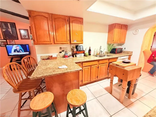 Kitchen with light stone countertops, a peninsula, a kitchen bar, wood finish cabinets, and light tile patterned floors