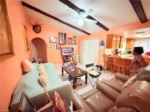 Living area with beam ceiling, light tile patterned floors, and a ceiling fan