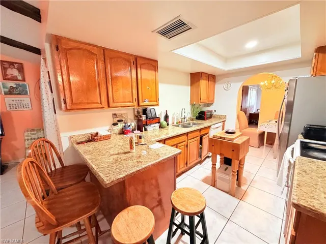 Kitchen with arched walkways, wood finish cabinets, a kitchen bar, light stone counters, and a raised ceiling