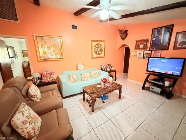 Living area featuring arched walkways, ceiling fan, tile patterned flooring, a textured ceiling, and beam ceiling