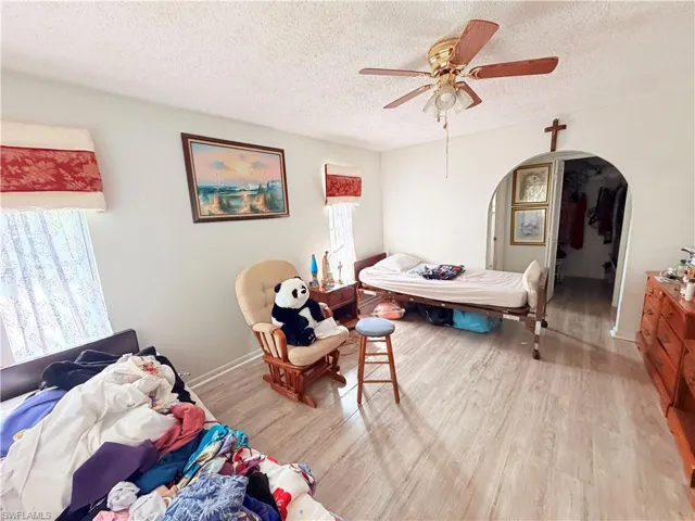 Bedroom featuring wood finished floors, arched walkways, a textured ceiling, and ceiling fan