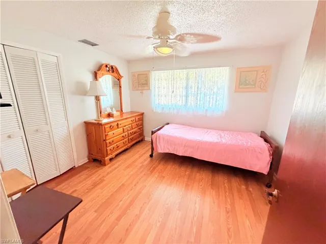 Bedroom with light wood finished floors, ceiling fan, a textured ceiling, and a closet