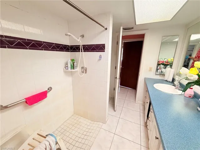 Bathroom featuring vanity, tiled shower, and light tile patterned floors