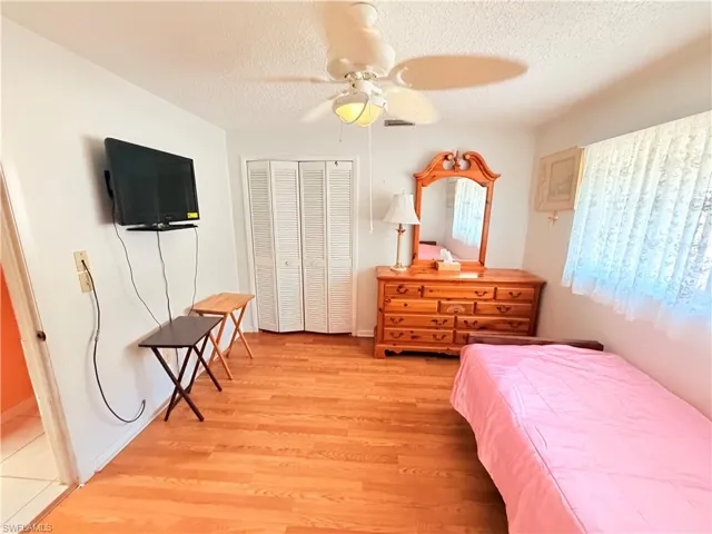 Bedroom with light wood-style floors, a textured ceiling, a ceiling fan, and a closet