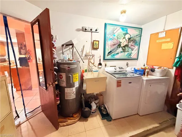 Laundry area featuring light tile patterned floors, electric water heater, and washing machine and clothes dryer
