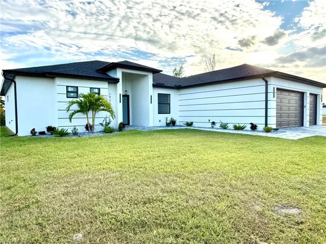 View of front of house with an attached garage, a front lawn, and stucco siding