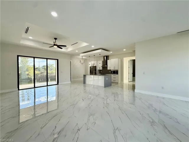Unfurnished living room featuring a raised ceiling, light marble finish flooring, recessed lighting, and a ceiling fan