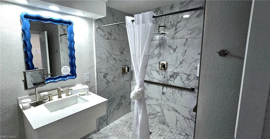 Bathroom with a textured wall, a marble finish shower, and vanity
